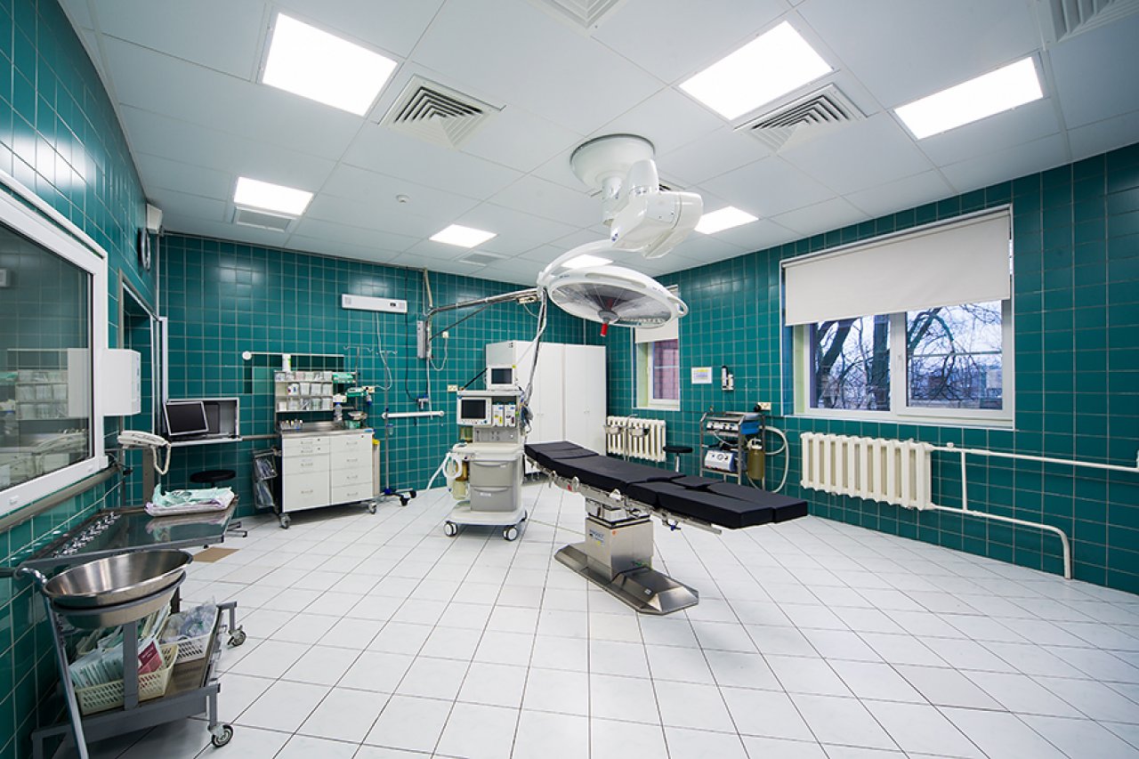 Slimnīcas iekštelpas, operācijas galds centrā, blakus iekārtas un monitori