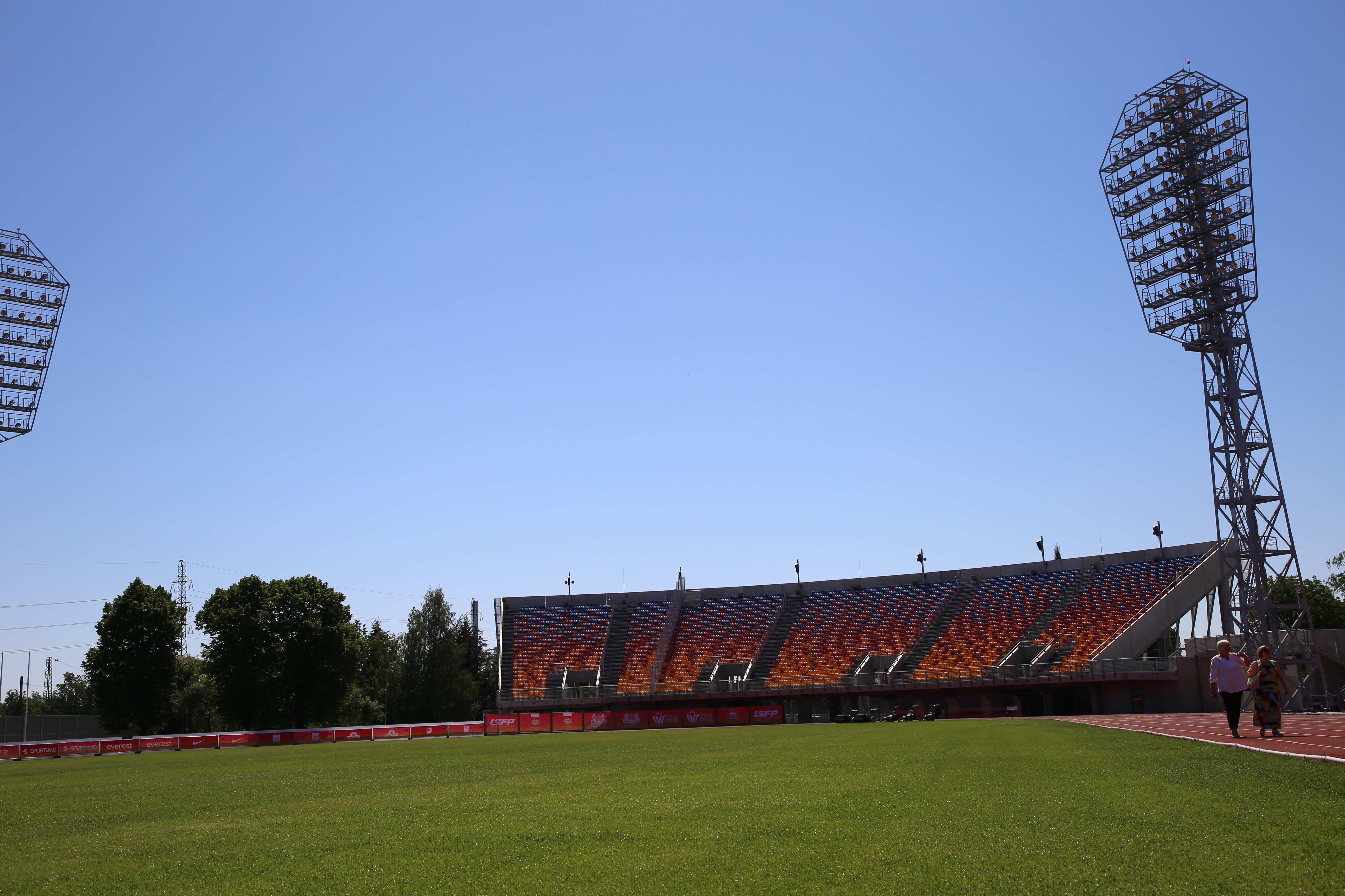 Foto: Atjaunotais Daugavas stadions, sieviešu pāris staigā pa skrejceļu labajā pusē, futbola laukums