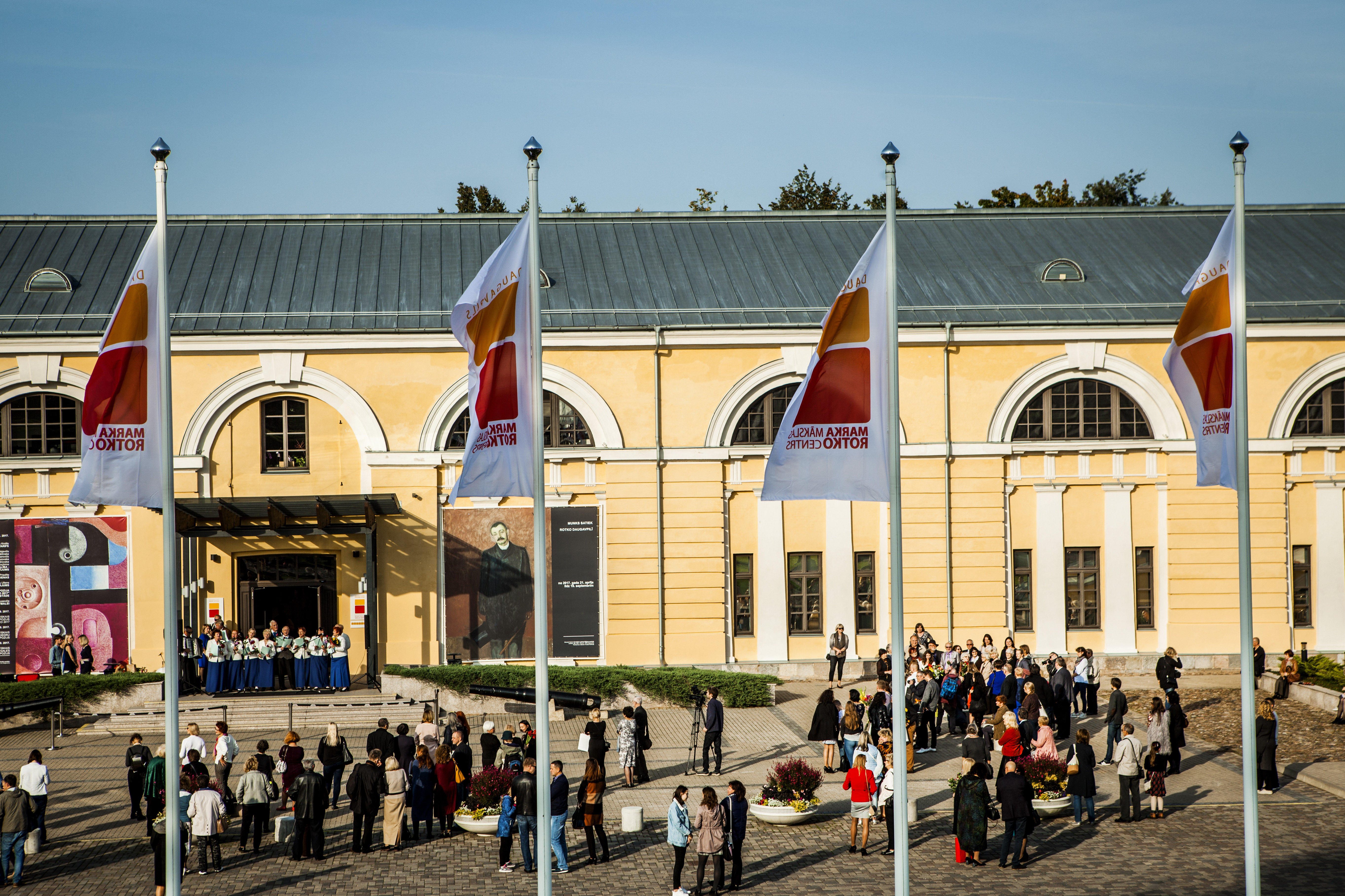 Daugavpils Marka Rotko mākslas centrs, āra pagalms ar četriem baltiem karogiem, kuri plīvo un uz kuriem izdrukāts centra logo