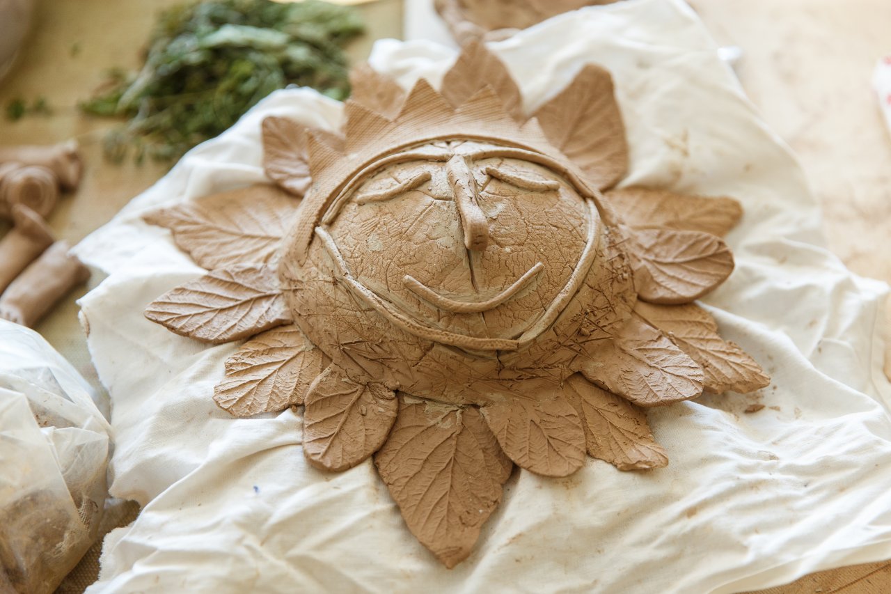 Rokdarbs - saule no māla ar smaidīgu seju un koku lapām no māla kā stari