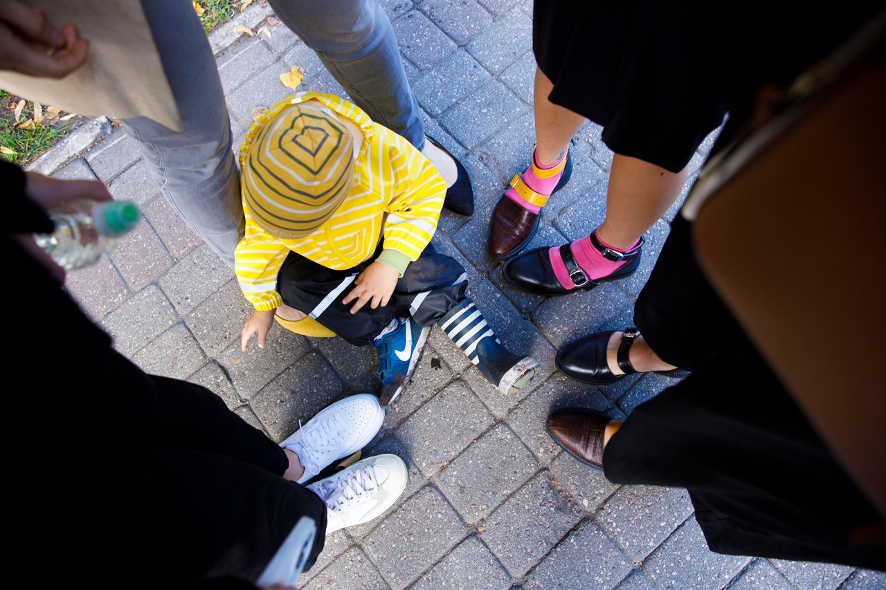 Legs of servereal people wearing mismatched shoes and a little kid sitting inbiteen